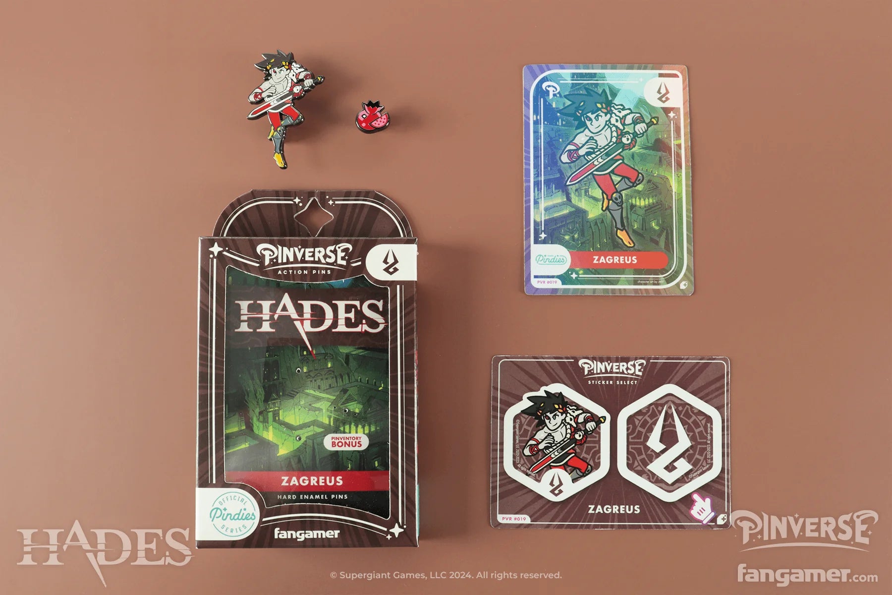 Pinyverse Zagreus collectible items including a card, pin, and packaging on a brown background.